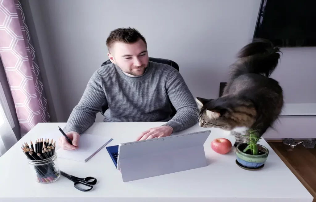 Mann teilt sich im Homeoffice Tisch mit Katze